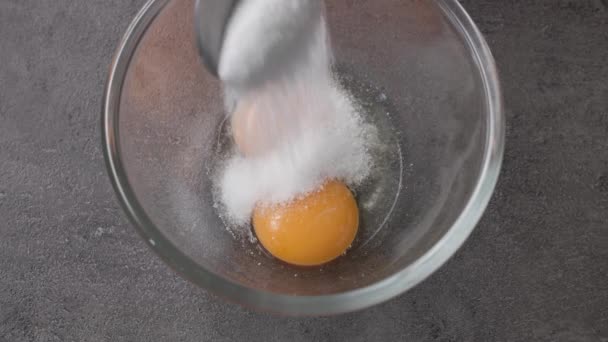 クックは ガラスボウルで生卵黄にスプーンと砂糖を追加します トップビュー 食品のクローズアップ — ストック動画