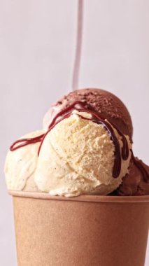 Çikolata sosu ve vanilyalı dondurma kepçeleri kağıt üzerinde akarken hafif arka planda dönen bardakları alır götürür. Tatlı tatlı, dönüşümlü yakın çekim. 4K 