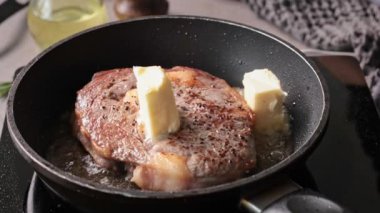 Bir şef mutfakta bifteğe tereyağı, biberiye ve sarımsak ekler. Lezzetli bir bifteği pişirme süreci, yiyeceklere yakın çekim.