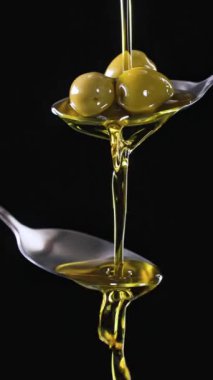 Siyah arka planda metal kaşıktan akan zeytinyağı. Yemek yakın çekim, ağır çekim, dikey video 4K