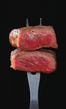 Siyah arka planda izole edilmiş bir çatalda taze ızgara biftek eti. Yiyeceklere yakın çekim
