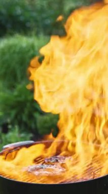 Arka planda yanan bir ızgaranın çok büyük bir alevi var. Barbekü et kızartması.