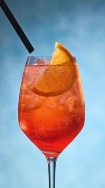 Portakal dilimli aperol spreyli kokteyl ve mavi arka planda saman. Kokteyl kamışı bardağa konur, yaz içkisinin yakınına.