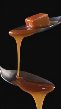 Erimiş karamel sosu siyah arka planda metal kaşıktan akıyor. Yemek yakın çekim, ağır çekim, dikey video 4K
