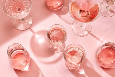 Güneşli pembe arka planda çeşitli kokteyl bardakları, üst manzara