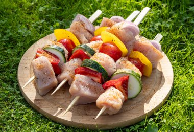 Taze çiğ tavuk eti ve ahşap kesme tahtasındaki sebze şişleri ızgara için hazır.