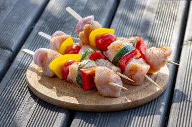 Taze çiğ tavuk eti ve ahşap kesme tahtasındaki sebze şişleri ızgara için hazır.