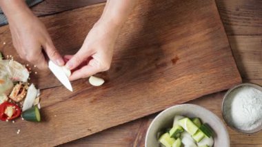 Şef, ahşap mutfak tahtasındaki bıçakla sarımsak kesiyor. Sağlıklı bir akşam yemeği için. Gazpacho çorbası yapma süreci