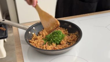 Aşçı mutfakta sıcak tavada domuz pastırması ve erimiş tereyağına maydanoz koyar ve karıştırır. Ev yapımı yemek yapma, evde yemek pişirme, yakın çekim.