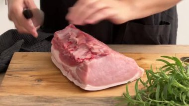 Aşçı mutfak tahtasının üzerinde bıçakla domuz pirzolası kemiklerini temizler. Ev yapımı yemek yapma, evde yemek pişirme, yakın plan yemek, domuz rostosu pişirme.