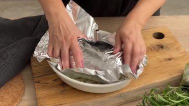 Aşçı, domuz pirzolasını ekmek kırıntıları, domuz pastırması ve tereyağı ile kaplıyor. Mutfaktaki tahta tahtada folyo var. Ev yapımı yemek yapma, evde yemek pişirme, yakın plan yemek, domuz rostosu pişirme.