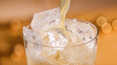 Taze portakal suyu bardağa buzla doluyor, yakın çekim. Odaklanmamış turuncu şenlik arka planı