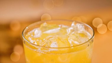 Taze portakal suyu bardakta buzlu, yakın çekim. Odaklanmamış turuncu şenlik arka planı