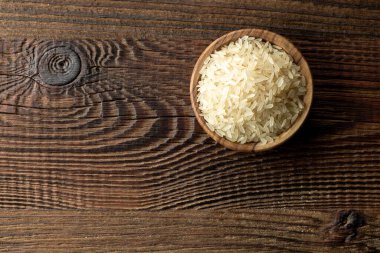 Kahverengi ahşap mutfak masasında çiğ pirinç kasesi.