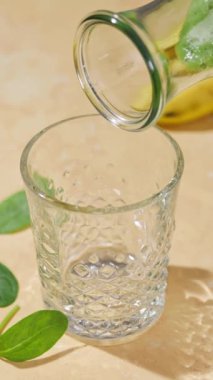 Taze yapılmış yeşil ıspanak ve muz suyu güneşli bir masa yüzeyindeki bir şişeden bir bardağa akıyor.