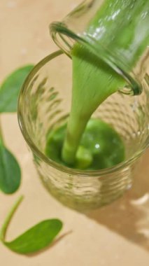 Taze yapılmış yeşil ıspanak ve muz suyu güneşli bir masa yüzeyindeki bir şişeden bir bardağa akıyor.