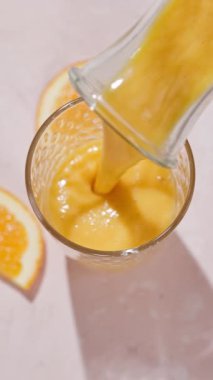 Taze yapılmış sarı turuncu ve mangolu smoothie güneşli bir masa yüzeyindeki bir şişeden bir bardağa akıyor.