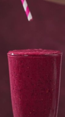 Bir bardak taze yapılmış kırmızı böğürtlen ve muzlu smoothie 'ye güneş ışığı masasında pipet koyar.