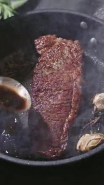 Şef, mutfakta tavada kızartılan sulu wagyu bifteğinin üzerine erimiş tereyağı ve yakın plan yemek koyar. Lezzetli biftek pişirme süreci.