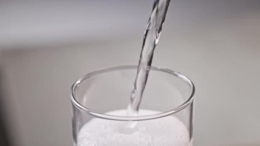 Köpüklü içeceğin kaplaması nötr bir arkaplanda bir bardağa akar ve köpük oluşturur..