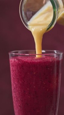 Kırmızı bir smoothie bardağı dönüyor ve bir şişeden içine sarı bir smoothie dökülüyor. Renkli yemekler, yakın plan.