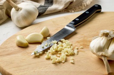 Taze çiğ sarımsak ve bıçak mutfak masasında tahta kesme tahtasının üzerinde. Fransız soğan çorbası yapma süreci, yakın plan yemek, sağlıklı yemek için sarımsak kesme.