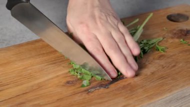 Sağlıklı vejetaryen yemeği yapmak ve yakın plan yemek için ahşap bir mutfak tahtasının üzerinde taze maydanoz yaprakları doğrayan bir şef.