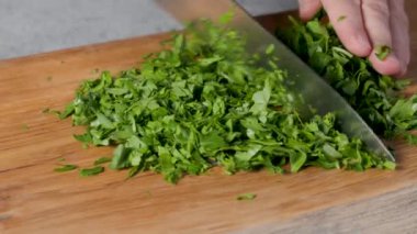 Sağlıklı vejetaryen yemeği yapmak ve yakın plan yemek için ahşap bir mutfak tahtasının üzerinde taze maydanoz yaprakları doğrayan bir şef.
