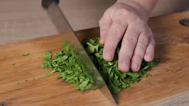 Sağlıklı vejetaryen yemeği yapmak ve yakın plan yemek için ahşap bir mutfak tahtasının üzerinde taze maydanoz yaprakları doğrayan bir şef.