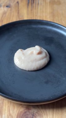 Fasulye sarımsaklı püre, sağlıklı bir vegan yemeği için ev mutfağında bir kaşıkla siyah bir tabağa konur. Yiyeceklere yakın çekim