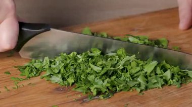 Sağlıklı vejetaryen yemeği yapmak ve yakın plan yemek için ahşap bir mutfak tahtasının üzerinde taze maydanoz yaprakları doğrayan bir şef.