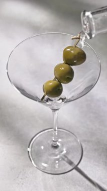 Votka martini kokteyli hazırlama süreci. Şeffaf sıvı bardağa dökülüyor. Güneşli restoran masasında zeytin var. Yakın plan için.