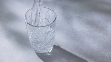 Gri, güneşli bir mutfak masasında bardağa dökülen temiz su, yavaş çekim.