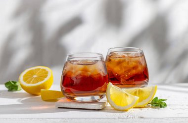 Güneşli beyaz ahşap masada iki bardak buzlu çay.