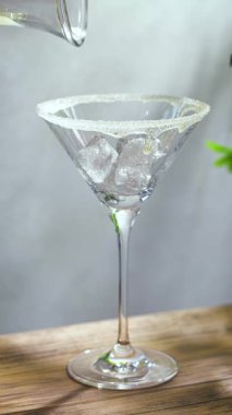Güneşli ahşap masada martini bardağında pina colada kokteyli hazırlama ve arka planda gri duvar.