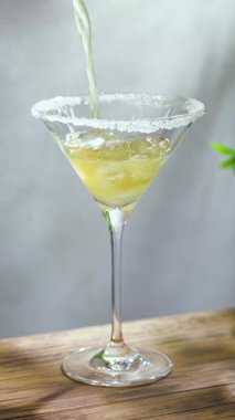 Güneşli ahşap masada martini bardağında pina colada kokteyli hazırlama ve arka planda gri duvar.