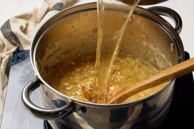 Kavanozdaki karamelli soğana et suyu ekle. Fransız soğan çorbası, yakın plan yemek, sağlıklı yemek için soğan ve sarımsak pişirme süreci