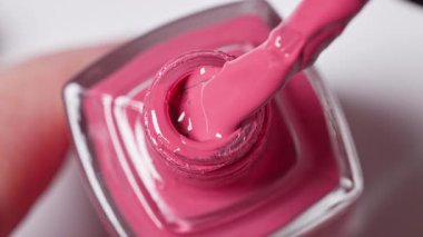 Beyaz arka planda pembe tırnak cilası şişesi ve pürüzsüz dokuyu, kozmetik ürünü yakın çekim makrosu ve üst görünümü gösteren bir fırça.