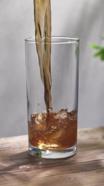 Taze köpüklü kola bardağa dökülüyor güneşli ahşap mutfak masasında ve gri duvar arkasında, yavaş çekim