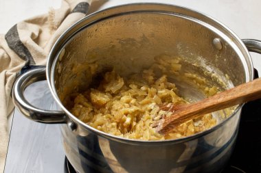 Un ile dilimlenmiş karamelli soğan bir tencerede ısıtılıyor. Fransız soğan çorbası, yakın plan yemek, sağlıklı yemek için soğan pişirme.