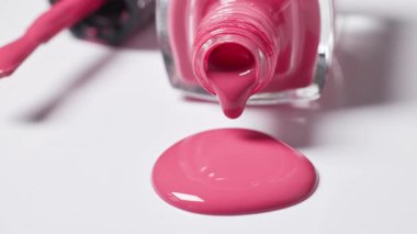Büyüleyici pembe tırnak cilası şişeden yavaşça beyaz bir yüzeye damlıyor, kozmetik yakın çekim makrosu.