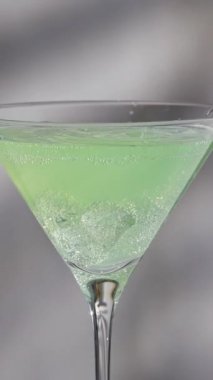 Martini bardağına dökülen buzlu yeşil sulu içecek ya da kokteyl gri mutfak masasına yavaş çekimde su sıçratır.