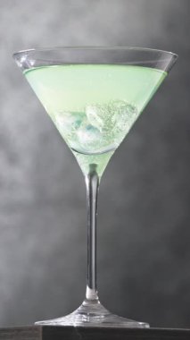 Bir bardak taze, yeşil, köpüklü içki şişeden çıkan buzlu martini bardağına dökülüyor.