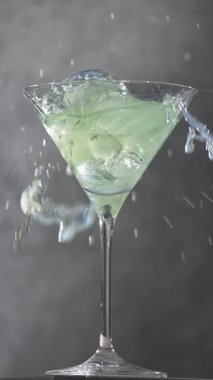 Buz küpü, martini bardağına dökülür. Buzlu yeşil sulu içecek ya da kokteyl yavaş çekimde gri bir mutfak masasına su sıçratır.