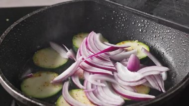 Aşçı, lezzetli ve sağlıklı bir yemek hazırlamak için kabak parçalarına taze kırmızı soğan ve sıcak yağda baharat koydu.