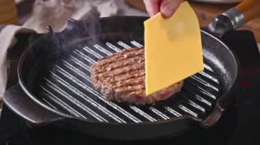 Aşçı, sıcak burger üzerinde erimek için peynir dilimi ızgara tavada pişirmek, yakın çekim yemek
