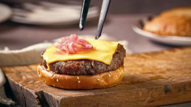 Aşçı ahşap kesme tahtasına lezzetli çizburger yapmak için ızgara hamburger etinin üzerine marine edilmiş kırmızı soğan dilimleri koydu.