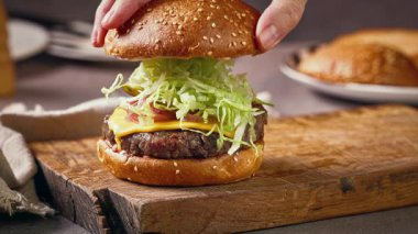 Şef, ev mutfağında lezzetli bir biftek burgeri hazırlıyor, ahşap bir tahtanın üzerinde, yemek yakın plan.