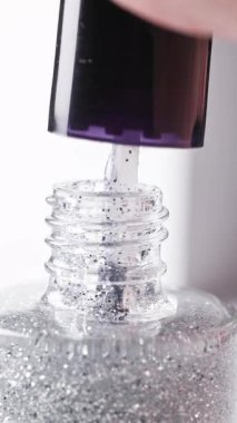 Beyaz arka planda parlayan şeffaf tırnak cilası şişesi ve pürüzsüz dokuyu gösteren bir fırça, kozmetik ürünü kapanış makrosu