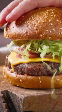 Aşçı, ahşap kesme tahtasına lezzetli çizburger yapmak için ızgara burgerin üzerine doğranmış marul koydu.